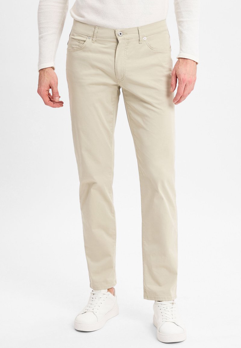 Beige katoenen broek met een rechte snit, voorzien van zijzakken en een ritssluiting, gecombineerd met witte sneakers. Eenvoudig, strak ontwerp.