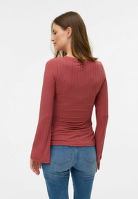 Maglietta a maniche lunghe a coste in rosa tenue con una silhouette aderente e maniche svasate. Abbinata a jeans in denim blu, vista da dietro.