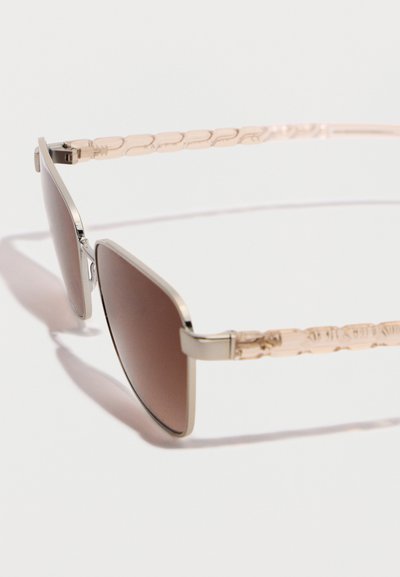 Γυαλιά ηλίου με τετράγωνα καφέ φακούς και ελαφριά χρυσά μεταλλικά μπράτσα με υφή σε λευκό φόντο.