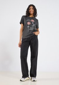 Svart t-shirt med blommig grafiktryck i rosa och vit text, matchad med svarta vida byxor och flerfärgade sneakers.