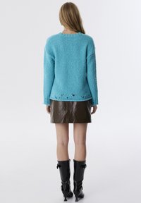 Türkisfarbener, flauschiger Strickpullover mit rundem Ausschnitt und gerippten Bündchen, ausgestattet mit einem dekorativen Saum und einem glänzenden Minirock aus braunem Leder.