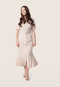 Robe boutonnée beige clair à manches courtes, avec taille ceinturée et jupe plissée. Tissu lisse avec une coupe ajustée et longueur genou.
