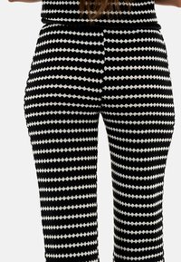 Leggings à motifs noir et blanc présentant un design géométrique avec des formes de losange alternées, un tissu texturé et une coupe ajustée.
