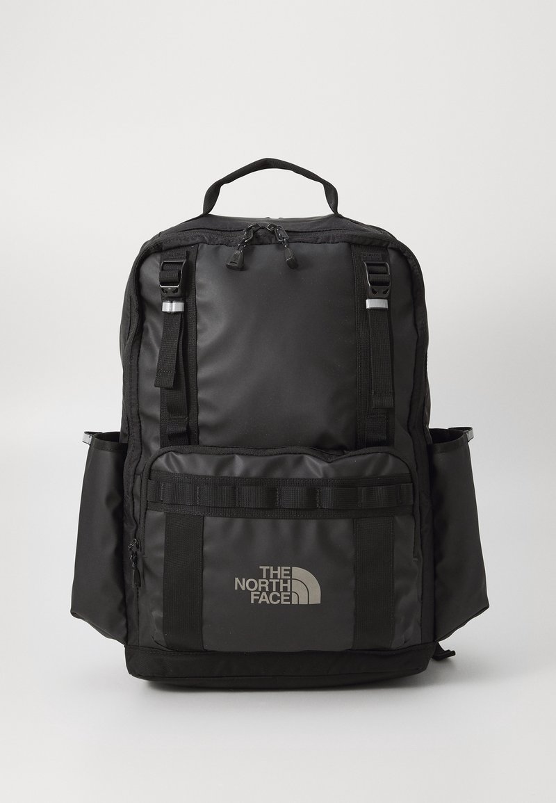 Sac à dos noir North Face avec plusieurs compartiments, poches latérales, bretelles réglables et poignée supérieure sur fond clair uni.