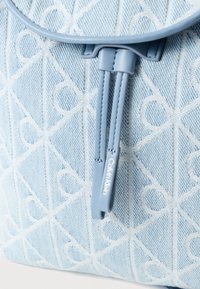 Σακίδιο πλάτης από ανοιχτό μπλε τζιν με μοτίβο διαμαντιού, δερμάτινες λεπτομέρειες και κορδόνι σύσφιξης με ετικέτα που γράφει «Calvin Klein».