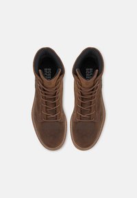 Pantofi înalți din suede maro, cu vârful rotund, design cu șireturi, suprafață texturată și talpă din cauciuc bej în contrast. Foderul interior este negru.