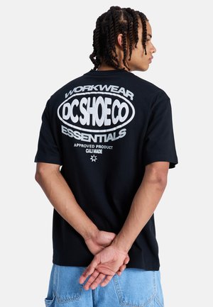 Czarny bawełniany t-shirt z dużym białym nadrukiem na plecach z tekstem "WORKWEAR DC SHOE CO ESSENTIALS". Krótkie rękawy i luźny krój.
