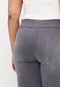 Gray fitted pants with a smooth texture, featuring a wide waistband and subtle stitching details along the back and seams.