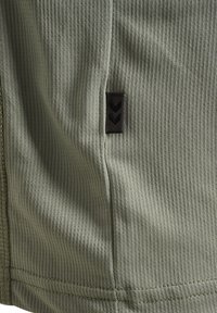 Olivgrön texturerad tyg med ett vertikalt ribbmönster. Inkluderar en liten svart etikett med chevronmönster på sömmen.