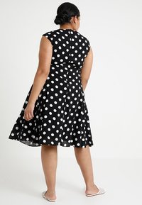 Vestido negro con lunares, con un corsé ajustado y falda acampanada. El diseño sin mangas cuenta con un escote redondo y dobladillo a la altura de la rodilla.