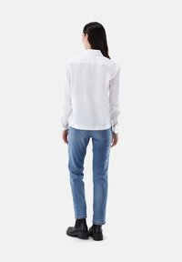 White long-sleeve shirt with a collar, paired with light blue jeans and black ankle boots. Smooth texture and fitted silhouette.