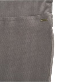 Grijze corduroy stof in een verticale ribbelpatroon met een klein gouden logo label. Gladde textuur, met stiksels langs de randen.