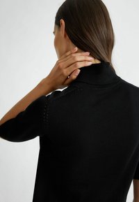 Pullover nero a maniche corte, realizzato in tessuto a maglia. Presenta un colletto alto e un sottile dettaglio perforato lungo le spalle.
