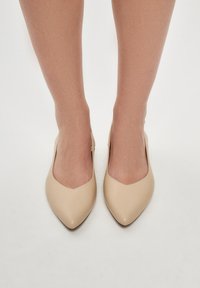 Beige ballerinat, joissa on sileä synteettinen päällinen ja matala korko, sekä edessä tyylikäs V-leikkaus.