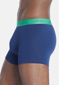Boxer brev per uomo in tessuto blu navy con elastico verde sulla vita, che presenta il logo "adidas". Il design è aderente con cuciture lisce.