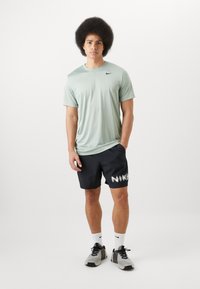 Maglietta sportiva verde chiaro a maniche corte, abbinata a pantaloni corti neri con il testo bianco "NIKE". Scarpe sportive grigie e calzini bianchi.