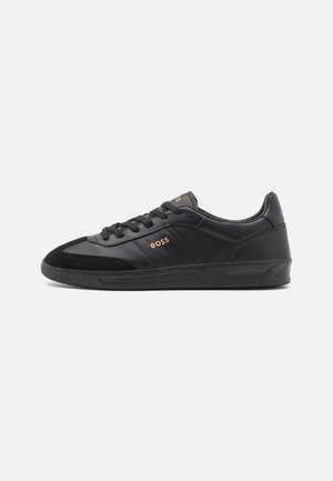 Baskets basses en cuir noir avec lacets noirs, semelle texturée et logo doré "BOSS" sur le côté et la languette.