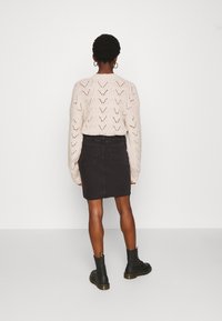 Suéter de punto color beige claro con un patrón en chevron, combinado con una falda de mezclilla negra y botines negros con suela gruesa.