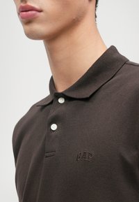 Καφέ πόλο μπλούζα από υφασμάτινη υφή, με γιακά, τριπλό κουμπί και διακριτό λογότυπο "GAP" κεντημένο στο στήθος.