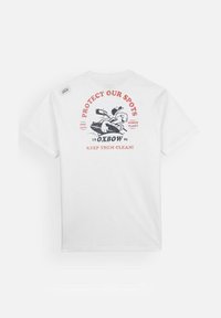 T-shirt en coton blanc avec une impression graphique au dos représentant un kayak et du texte en rouge et noir, mettant en avant la sensibilisation à l'environnement.