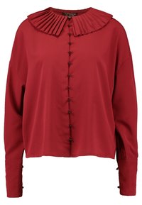 Blusa rossa con colletto plissettato, chiusura frontale con bottoni e maniche lunghe. Il materiale appare liscio; presenta bottoni neri e una vestibilità rilassata.