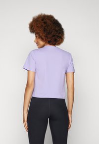 Tricou scurt din bumbac mov, cu mâneci scurte și guler rotund, purtat cu colanți negri. Textură netedă, design simplu.