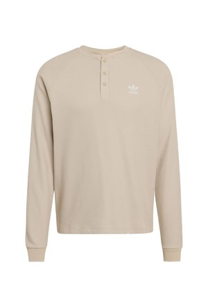 Beige pitkähihaine henley-paita, jossa on teksturoitu kangas, kolmen napin lista ja valkoinen logo vasemmassa rinnassa. Ribatut hihansuut ja kaulus.