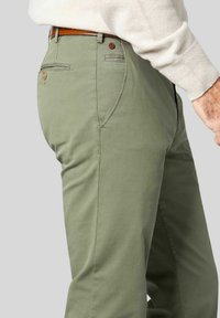 Grüne Baumwollchinos mit glatter Oberfläche, ausgestattet mit seitlichen Taschen, einer hinteren Tasche mit Knopf und einem braunen Gürtel. Maßgeschneiderte, gerade Beinform.