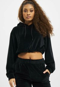 Crni skraćeni hoodie izrađen od mekog, teksturiranog baršuna s kapuljačom na vezanje. Ima duge rukave i suženi donji rub. Uparen s matching hlačama.