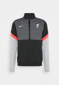Jackett bicolor en gris y negro con acentos rojos, dobladillo elástico, cuello alto, cierre frontal, presenta el logo del Liverpool FC y el swoosh de Nike.