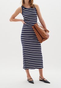 Robe sans manches à rayures bleu marine et blanches avec un design ajusté, texture côtelée et fente sur le côté. Sac fourre-tout marron au forme douce et structurée.