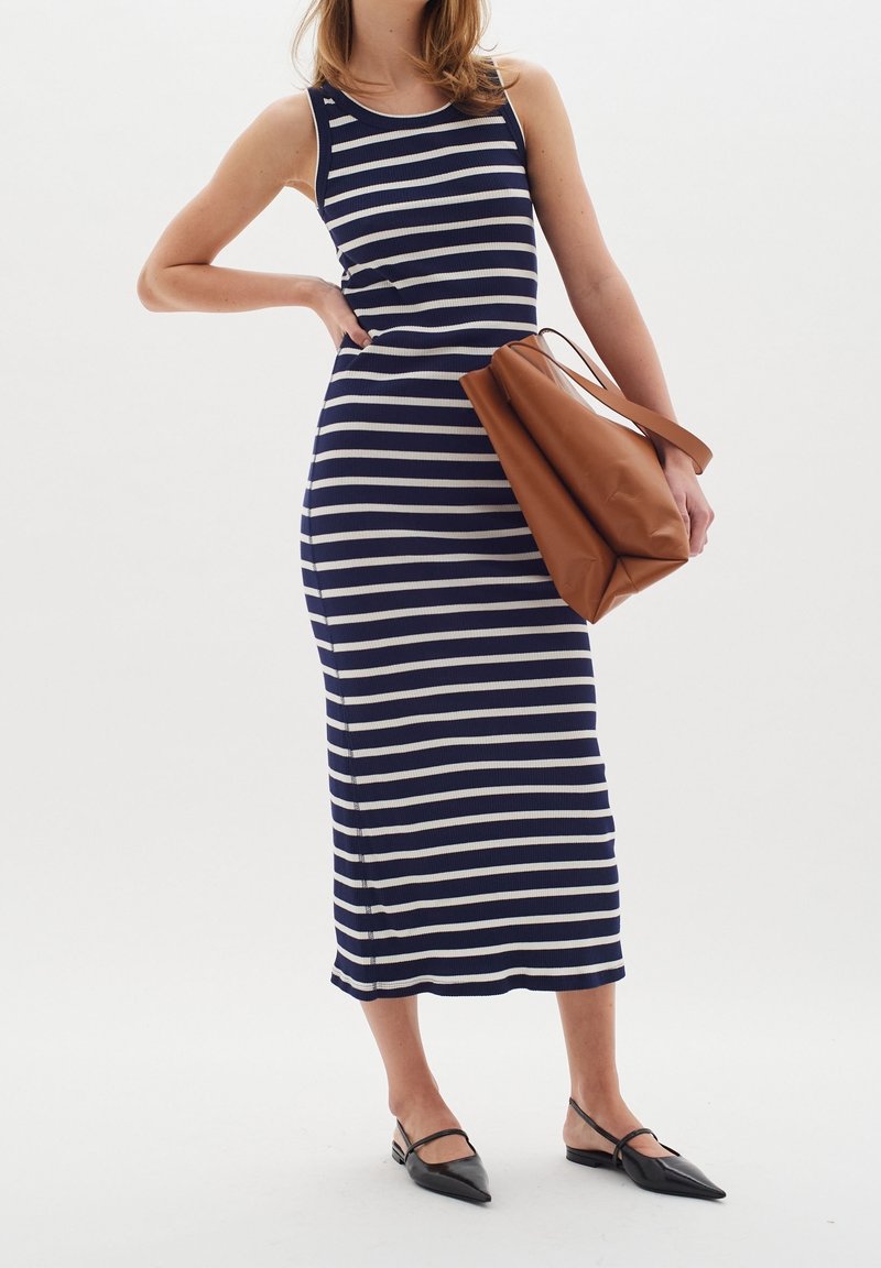 Robe sans manches à rayures bleu marine et blanches avec un design ajusté, texture côtelée et fente sur le côté. Sac fourre-tout marron au forme douce et structurée.