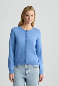 Hellblauer Cardigan aus weichem Strickstoff, mit runder Halslinie, langen Ärmeln und dekorativen Knopfverschluss. Subtile Musterdetails.