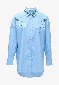 Camisa abotonada de color azul claro con adornos florales en verde esmeralda y pequeños remaches. Presenta un collar clásico y mangas largas.