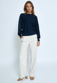 Marineblauer oversized Pullover mit langen Ärmeln, kombiniert mit beigen, hoch taillierten, weit geschnittenen Hosen und braunen Blockabsatzsandalen. Schlichtes Design.