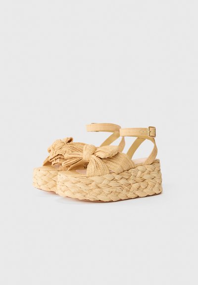 Yellow woven platform sandals with a knotted strap design, featuring an espadrille-style woven sole and adjustable ankle straps.