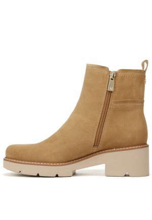 Bottine en suède beige avec une fermeture éclair sur le côté, un bout carré et un talon épais beige. Présente une semelle cousue et une petite languette à l'arrière.