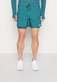 Teal löpshorts med svart dragsko, snabbtorkande material, innertyg och sidofickor. Har en vit Nike-logga på framsidan.