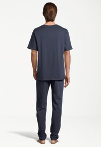 Marineblauwe katoenen pyjama set met een T-shirt met korte mouwen en lange broek, met een eenvoudig ontwerp en ontspannen pasvorm, gezien vanaf de achterkant.