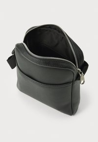 Sac en cuir noir à bandoulière avec une fermeture éclair, une poche avant et des détails de couture texturée. Fini lisse avec un design simple.