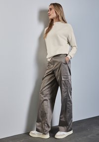 Felpa beige chiaro abbinata a pantaloni cargo grigi scuri, larghi e lucidi, con tasche laterali, completati da chunky sneakers bianche.