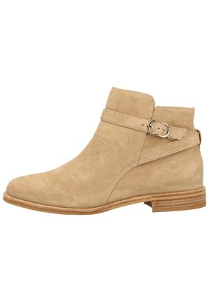 Bottine en daim beige à bout rond, avec une sangle décorative et une boucle, et un talon en bois empilé. Texture lisse avec un design minimaliste.