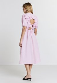 Abito rosa a righe con maniche a sbuffo corte e schiena scoperta, con un dettaglio di fiocco. Tessuto morbido, design lungo fino al ginocchio, abbinato a tacchi neri.