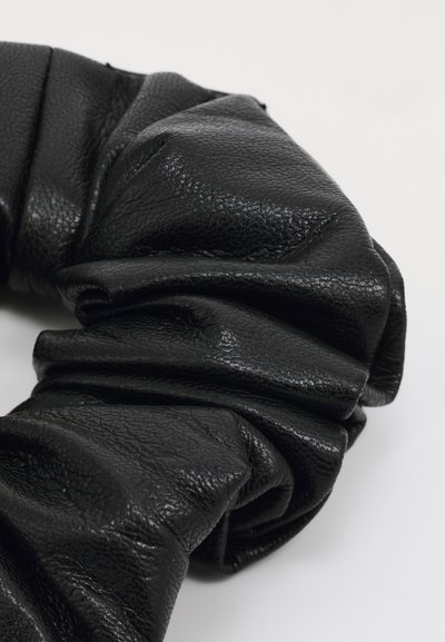 Melnas ādas scrunchie ar teksturētu, sarullētu virsmu, kas izceļ mīkstus salocījumus un spīdīgu apdari, izstrādāts matiem.