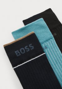 Drei Paar Socken: ein dunkelblaues Paar mit braunen und weißen Akzenten, ein tealfarbenes Paar mit vertikalen Streifen und ein einfarbig schwarzes Paar. Mit gerippter Textur.
