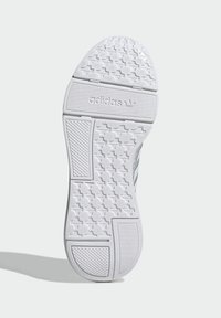 Fehér sneaker talp texturált gumival a tapadásért, Adidas márkajelzéssel, valamint kör- és négyzet alakú formákkal díszített mintázatú gumitalppal.