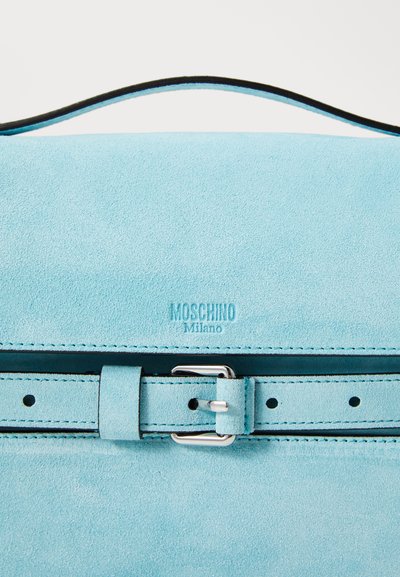 Light blue suede handbag with a black leather handle, featuring a silver buckle, embossed logo, and visible stitching details.
