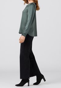 Blusa verde in satin a maniche lunghe con una vestibilità rilassata, abbinata a jeans neri a vita alta a palazzo e scarpe con tacco a punta nere.