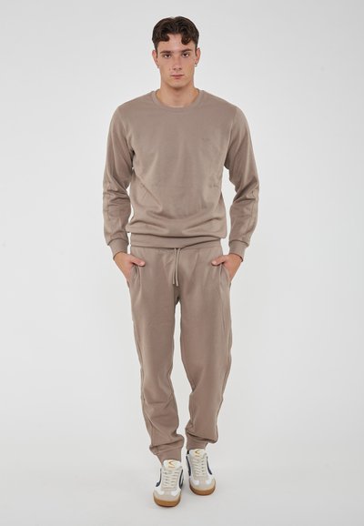 Maglione di cotone beige e pantaloni jogger, maniche lunghe, polsini a costine, vita elastica, due tasche laterali, abbinati a sneaker bianche e blu navy.