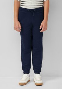 Marineblauwe trainingsbroek met een elastische tailleband en trekkoord, voorzien van taps toelopende boorden bij de enkels. Gestyled met witte sneakers.